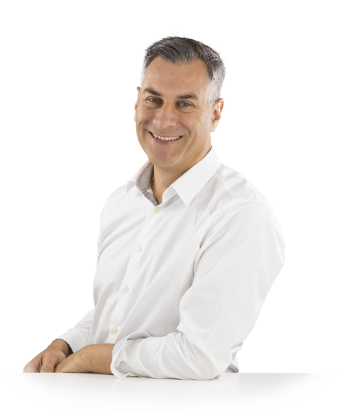 Jochen Muffler stands leaning against a table in a white shirt and looks into the camera with a smile.