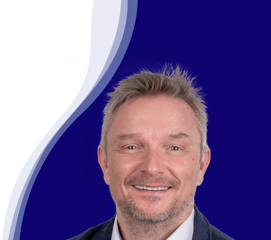Holger Geck, directeur du marketing et de la gestion des données produits chez Gust. Alberts, sourit à la caméra. Il a les cheveux courts, blond grisâtre et une courte barbe. Il porte une chemise blanche et une veste sombre. En arrière-plan, on peut voir une forme de vague incurvée en blanc, bleu clair et bleu foncé.
